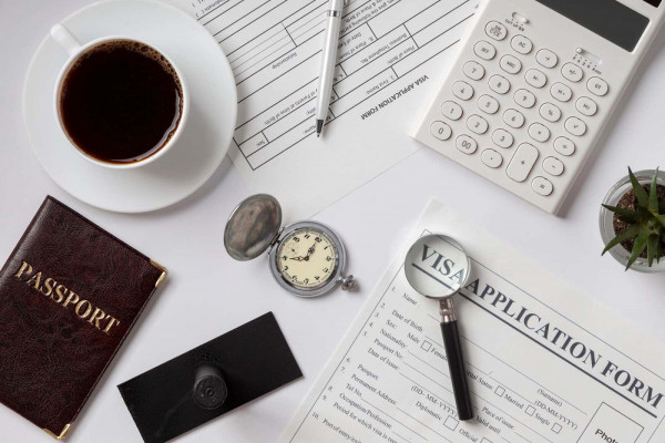 A cup of coffee, a Passport, and a calculator with a Visa Application Form on table