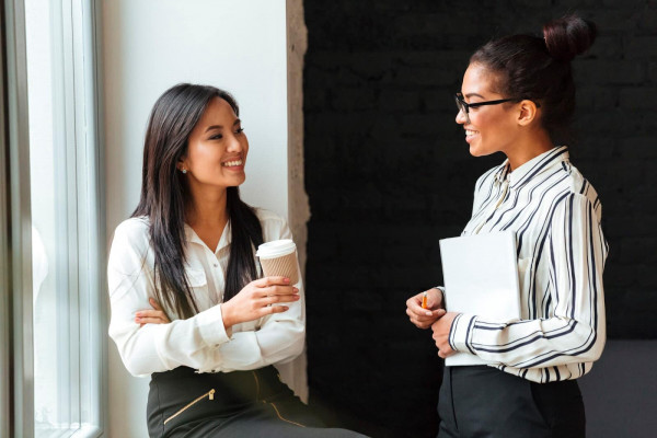 A lady holding a cup of coffee and smiling while talking with another lady