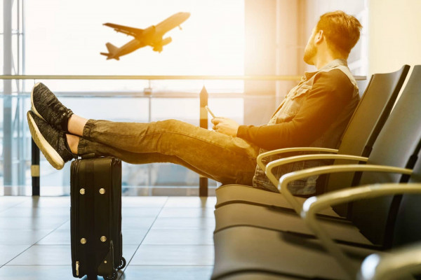 man-sitting-on-gang-chair-with-feet-on-luggage-looking-at-airplane